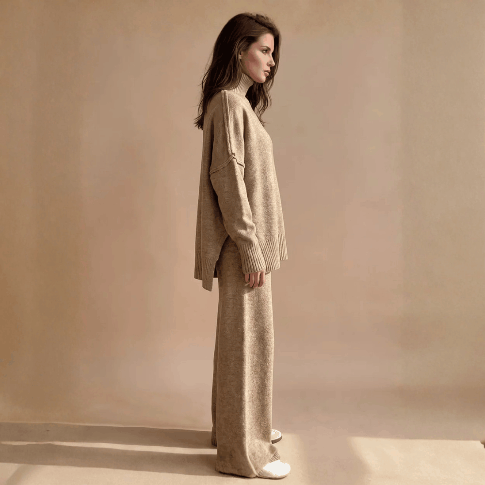 Full-length side profile view of a model wearing the beige oversized turtleneck lounge set showing the high-low side slit hem and relaxed fit pants.