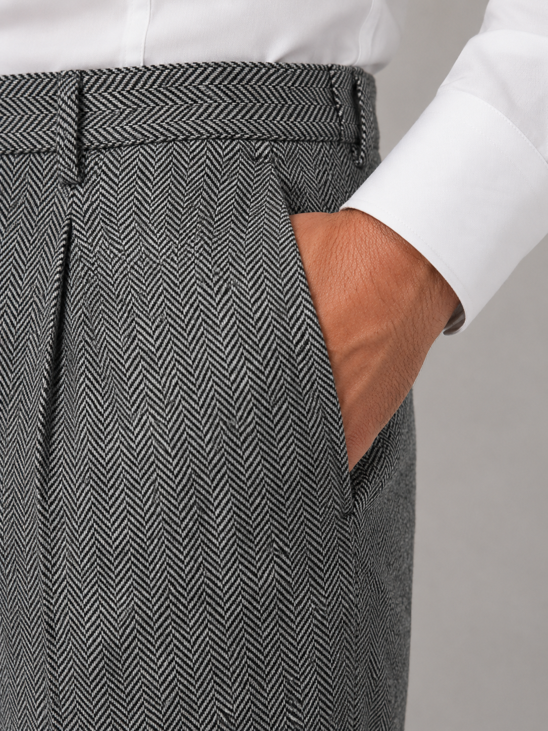 Gray herringbone trousers featuring a high-rise waist, front pleats, and side pockets worn with a white shirt.