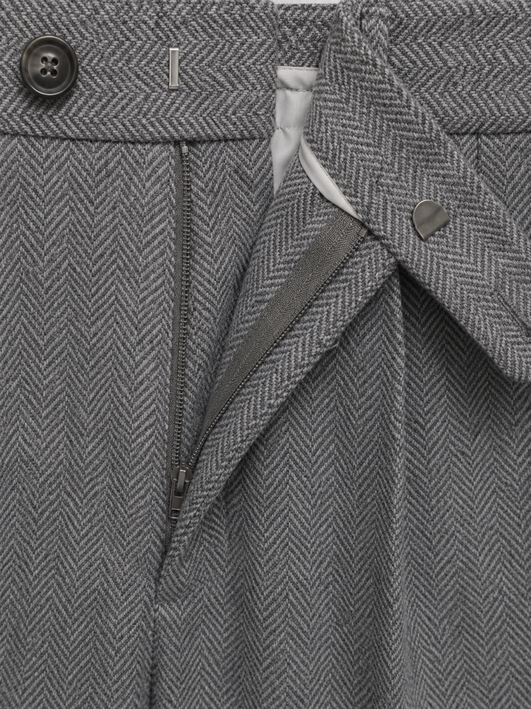 Gray herringbone trousers featuring a high-rise waist, front pleats, a sturdy zip fly, and a buttoned closure.