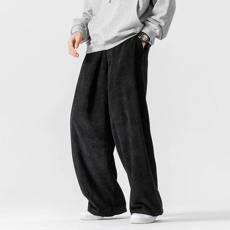 Black wide-leg corduroy pants featuring deep front pleats, a relaxed fit, and an adjustable drawstring waistband.