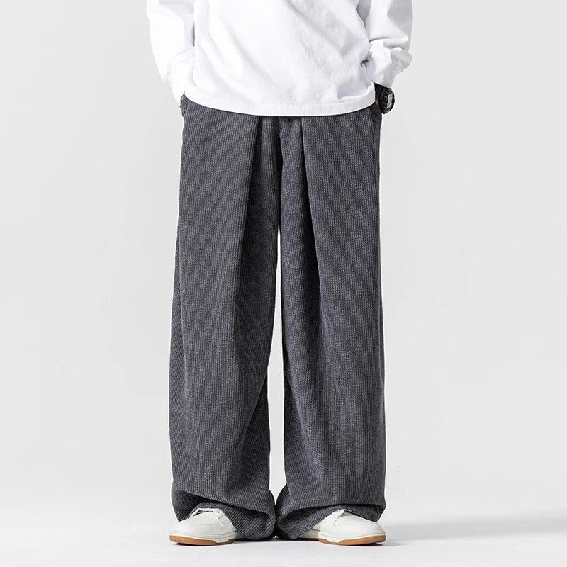 Charcoal gray wide-leg corduroy pants featuring deep front pleats, a relaxed fit, and a comfortable drawstring waist.
