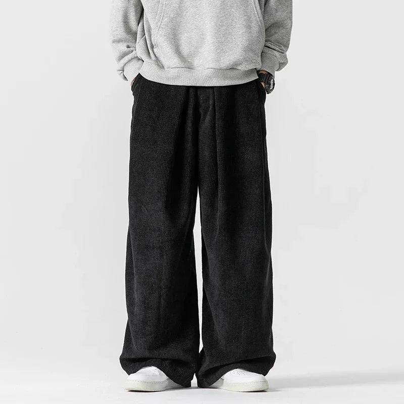 Black wide-leg corduroy pants featuring deep front pleats, a relaxed silhouette, and an adjustable drawstring waist.