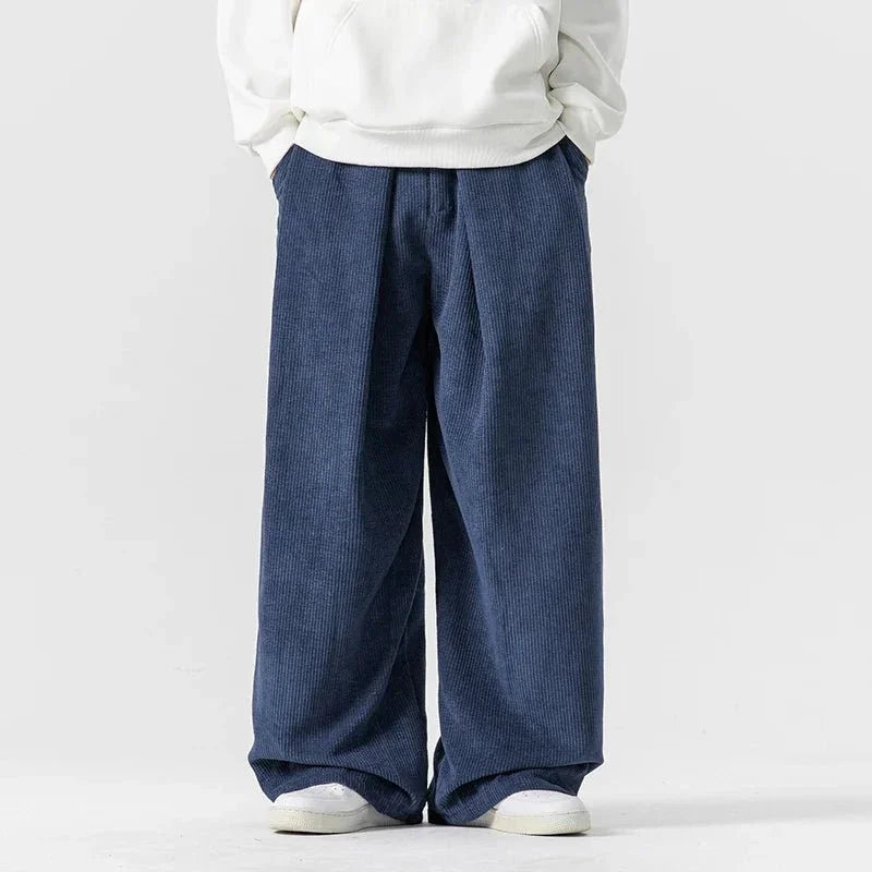 Navy blue wide-leg corduroy pants with front pleats, a relaxed fit, and a drawstring waist worn with a white hoodie.