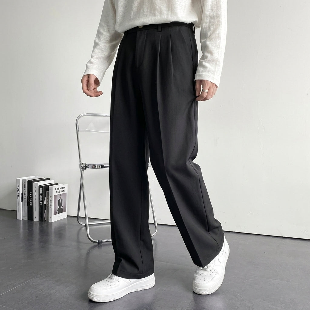 Black pleated wool trousers with a relaxed, full-length drape, styled with a white long-sleeve shirt and sneakers.