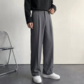 Charcoal gray pleated wool trousers with a relaxed, straight-leg fit and smooth drape, styled with a black long-sleeve top.