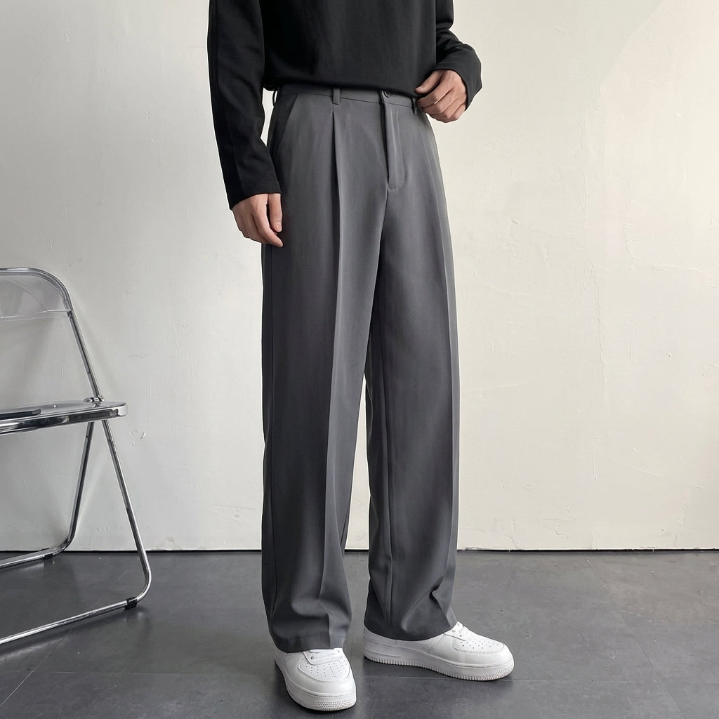 Charcoal gray pleated wool trousers with a relaxed, straight-leg fit and smooth drape, styled with a black long-sleeve top.