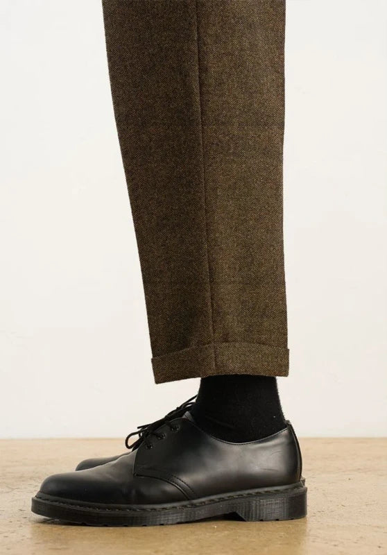 Side close-up view of the lower pant leg showing the cuffed hem detail of dark brown tweed dress pants paired with black socks and black leather oxford shoes.   