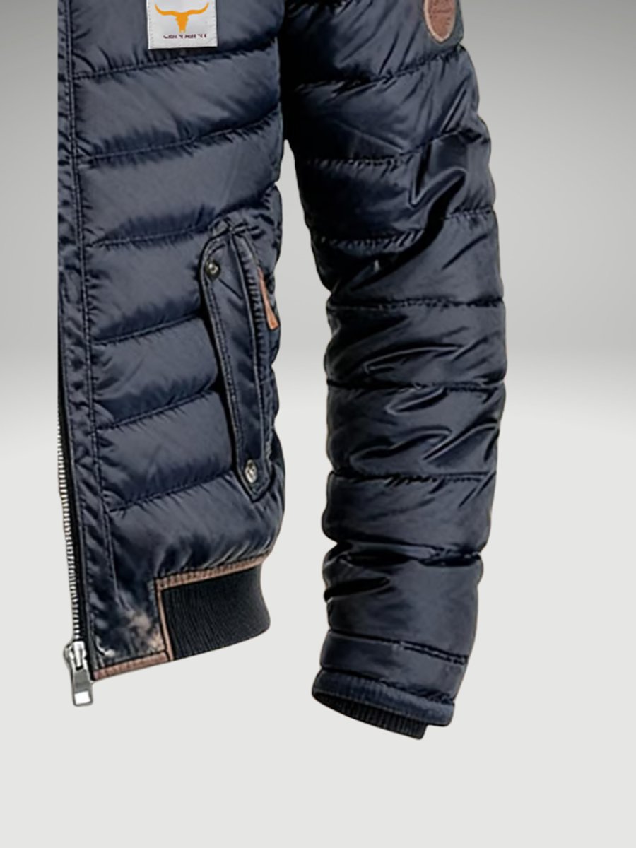 Navy blue quilted puffer bomber jacket with snap-flap chest pockets, contrast trim, and ribbed cuffs against a grey background.