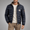 Navy blue quilted puffer bomber jacket with contrast stand collar, snap-flap chest pockets, and ribbed hem on a male model.