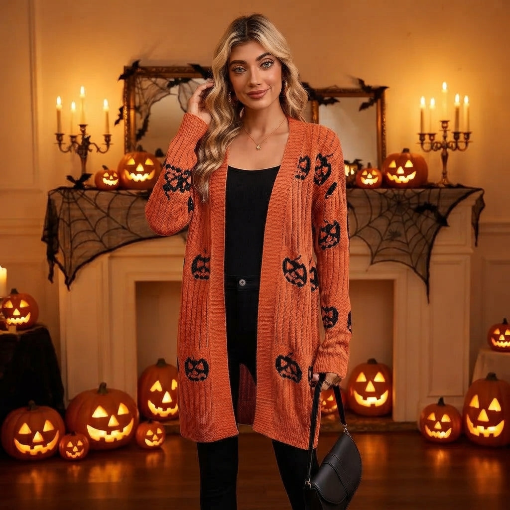 Model posing in the orange longline open-front pumpkin knit cardigan in a dimly lit Halloween setting with lit jack-o'-lanterns and candles