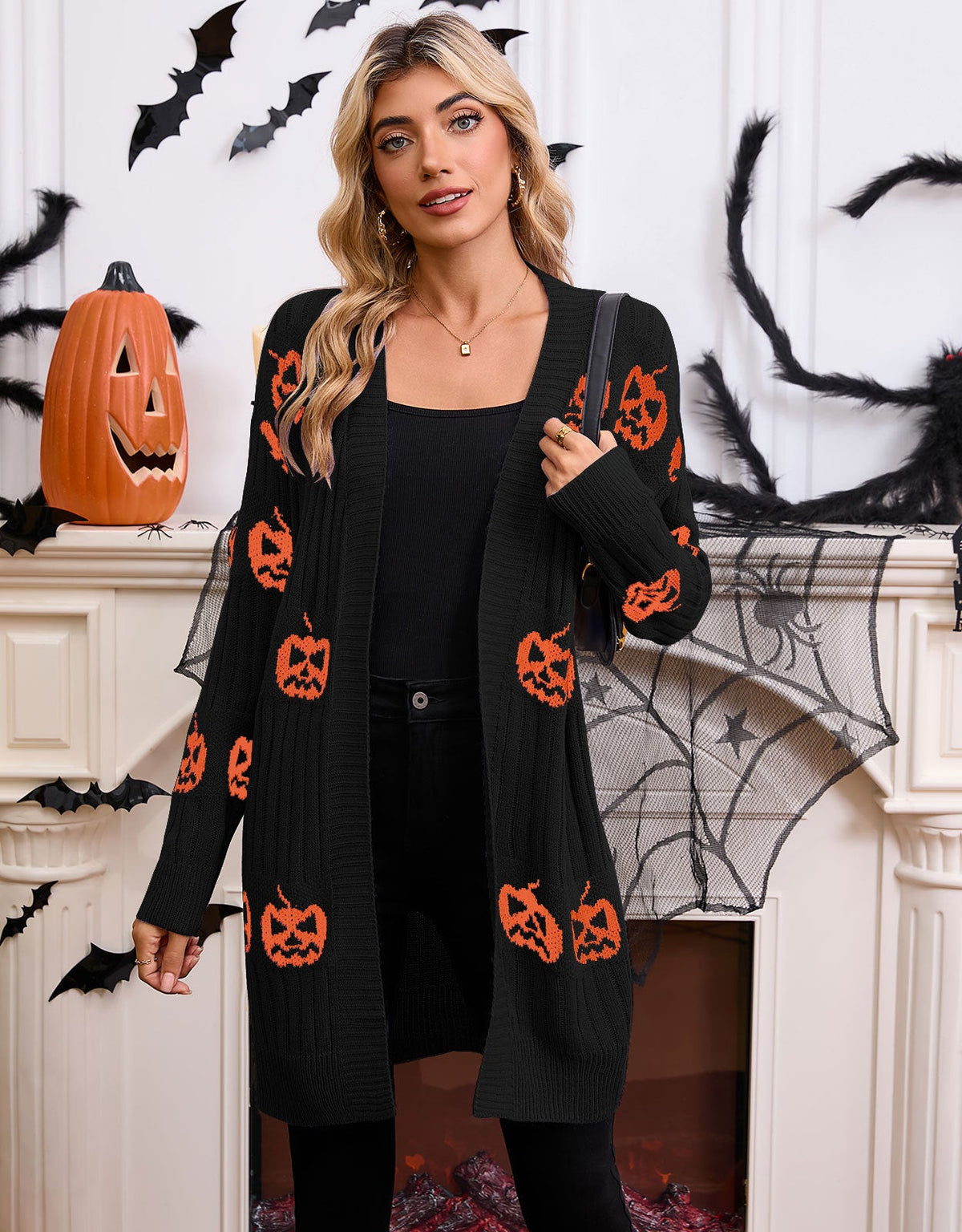 Full-length front view of a model wearing the longline open-front pumpkin knit cardigan in black with orange jack-o'-lantern motifs.