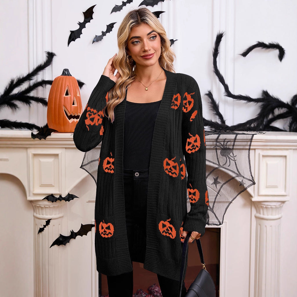 Three-quarter front view of a model wearing the black open-front longline knit cardigan featuring orange pumpkin graphics and front patch pockets.
