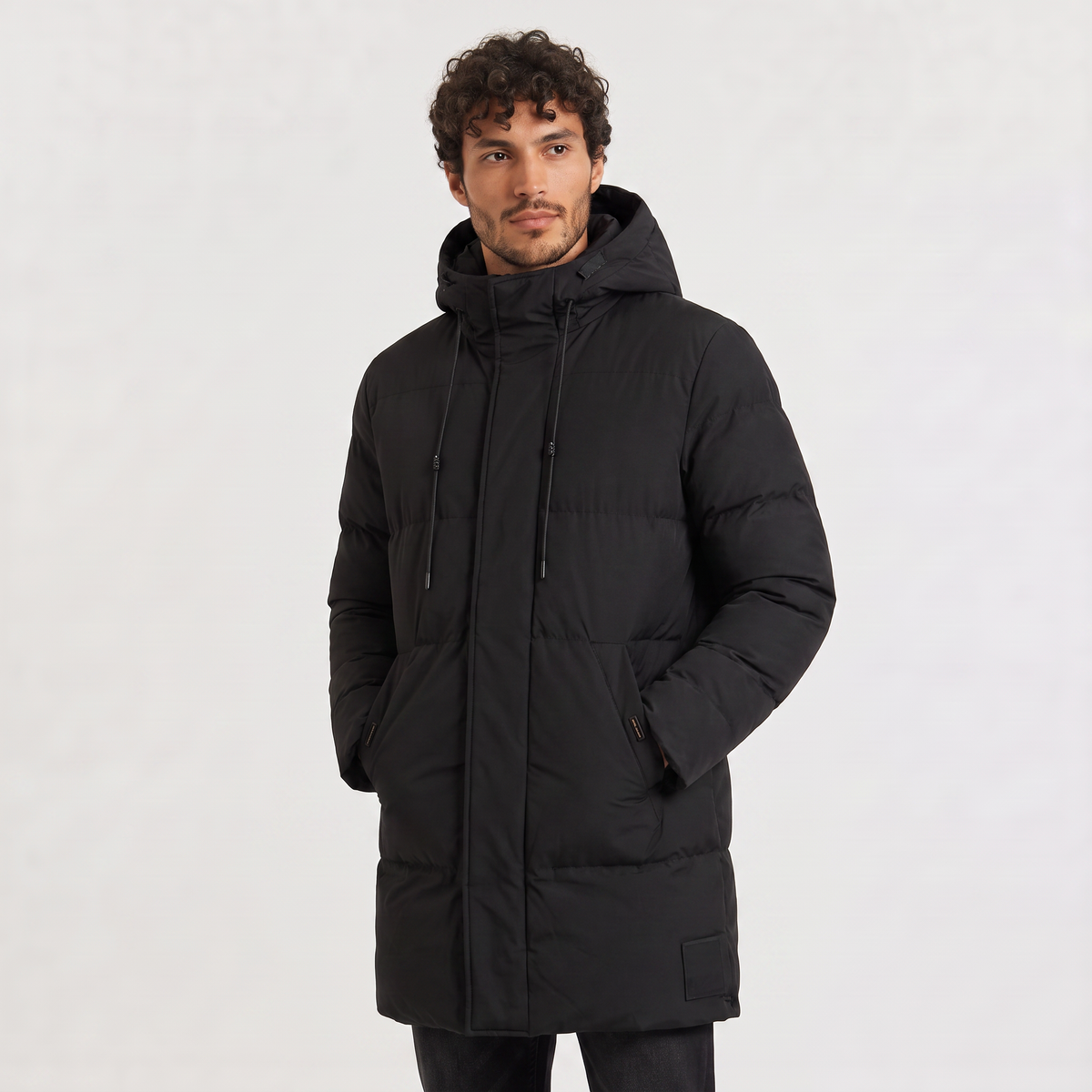 Black longline quilted parka with a drawstring hood and concealed zip placket, worn by a man against a neutral background.