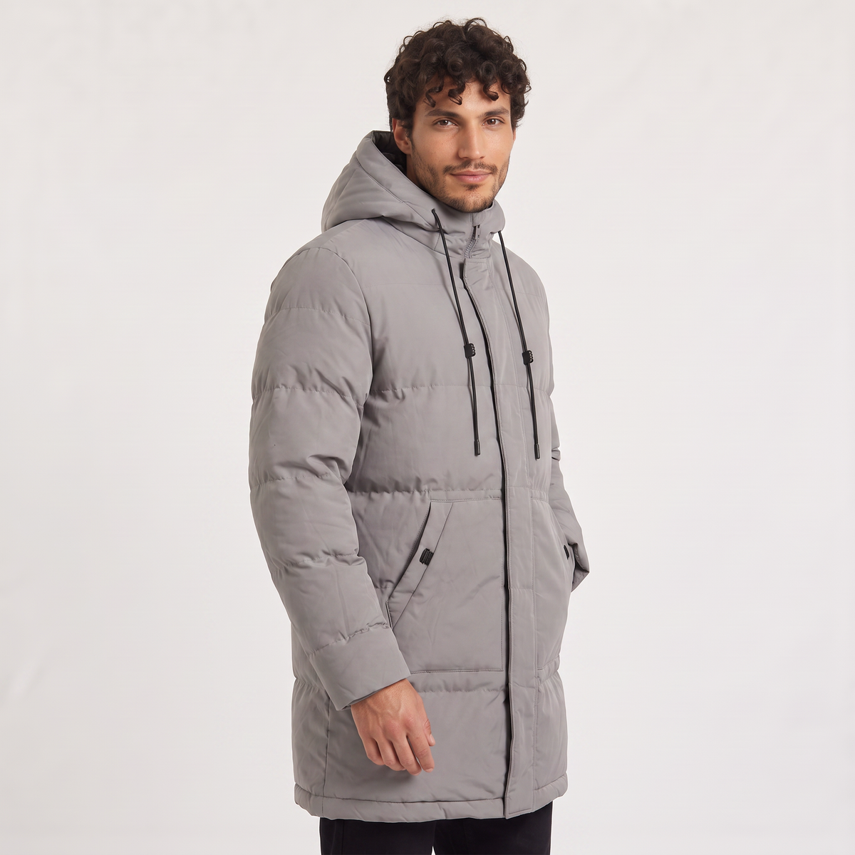 Gray quilted longline parka with a drawstring hood and concealed zip placket, worn by a man against a white background.