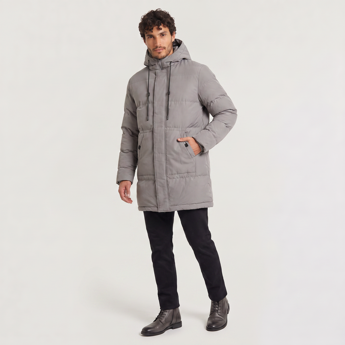 Gray quilted longline parka with a drawstring hood and concealed zip placket, worn over black trousers.