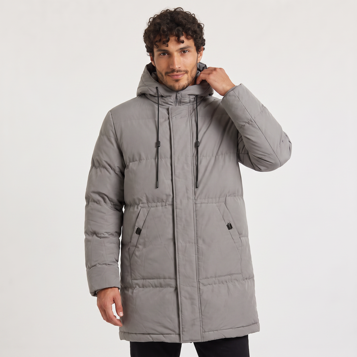 Gray quilted longline parka with a drawstring hood and concealed zip placket worn by a man against a white background.