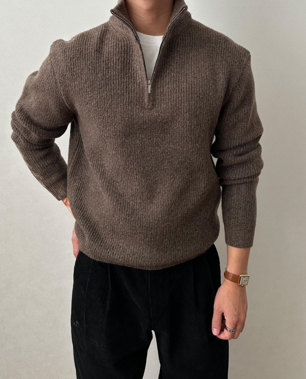 Brown quarter-zip knit sweater with a stand collar, ribbed cuffs, and a relaxed fit, styled with black trousers.