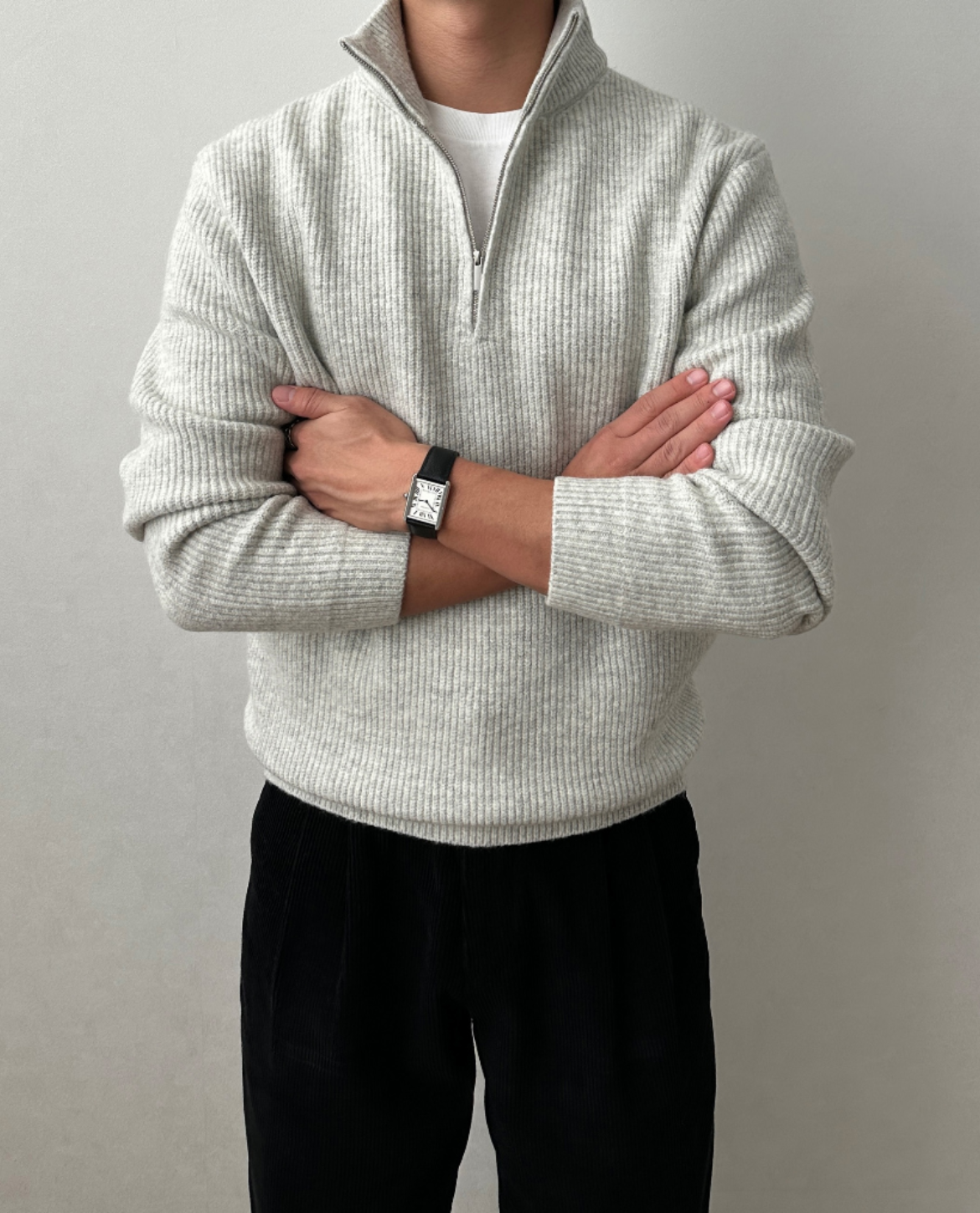Light gray quarter-zip knit sweater featuring a stand collar and ribbed texture, shown with arms crossed.