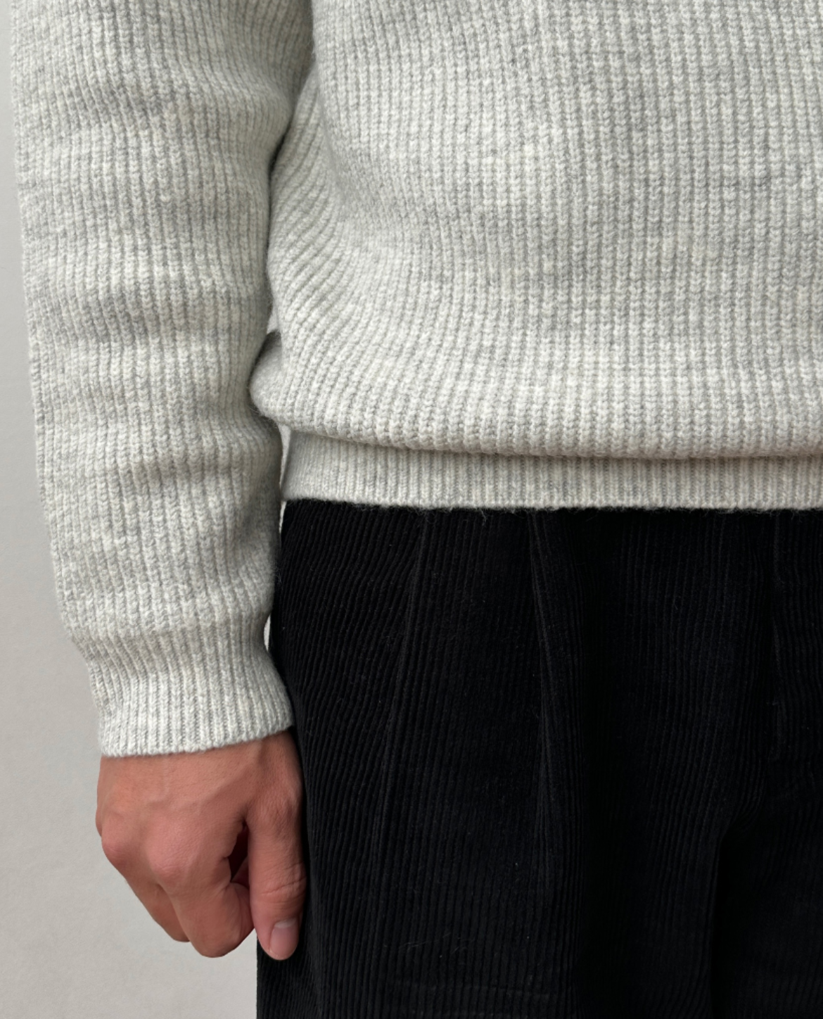 Close-up of the light gray knit sweater highlighting the soft ribbed texture, sleeve cuff, and hem.