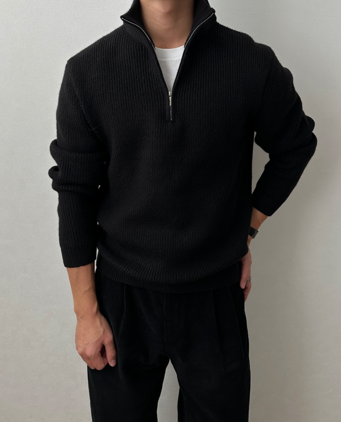 Black quarter-zip knit sweater with a stand collar, ribbed cuffs, and a relaxed fit, paired with black trousers.