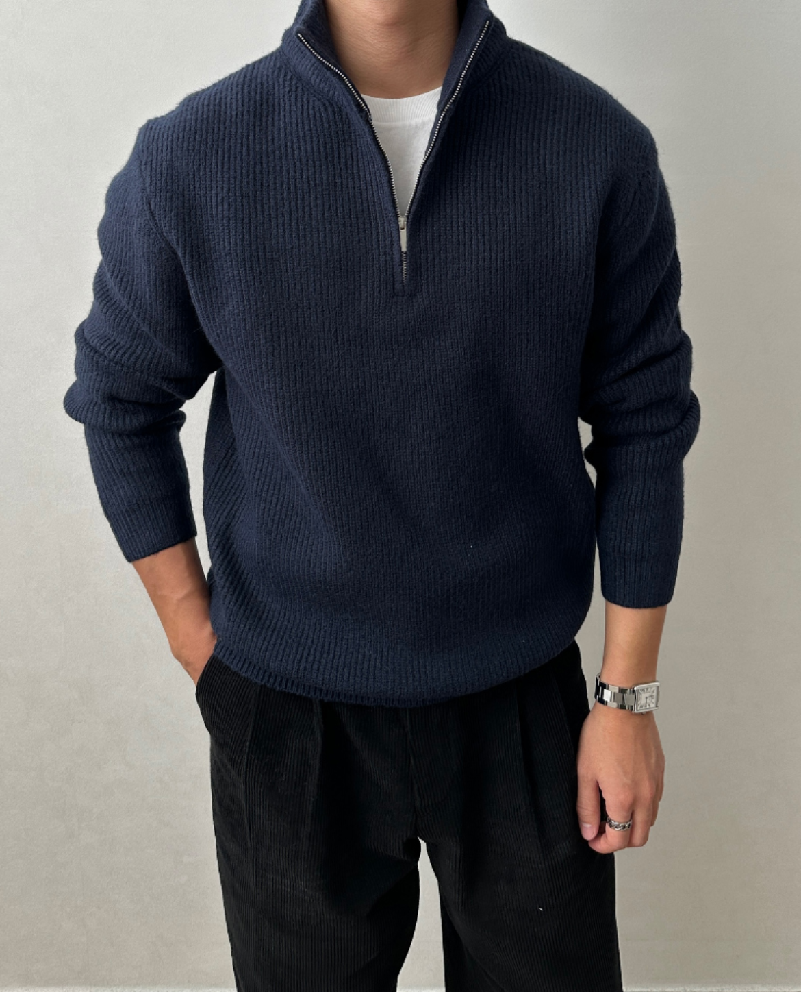 Navy quarter-zip knit sweater with a stand collar, ribbed cuffs, and a relaxed fit, paired with black trousers.