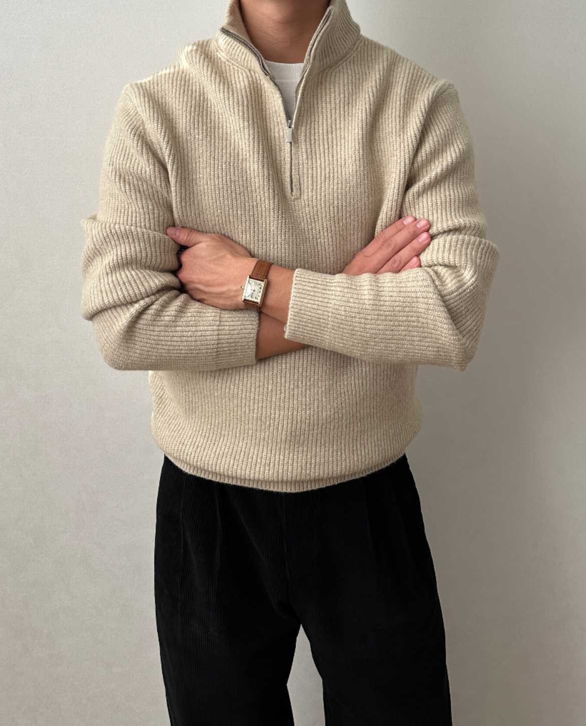 Cream quarter-zip knit sweater with a stand collar, ribbed cuffs, and a relaxed fit, shown with arms crossed.