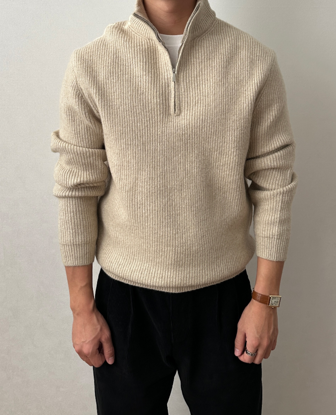 Cream quarter-zip knit sweater featuring a stand collar, ribbed cuffs, and a relaxed fit, paired with black trousers.