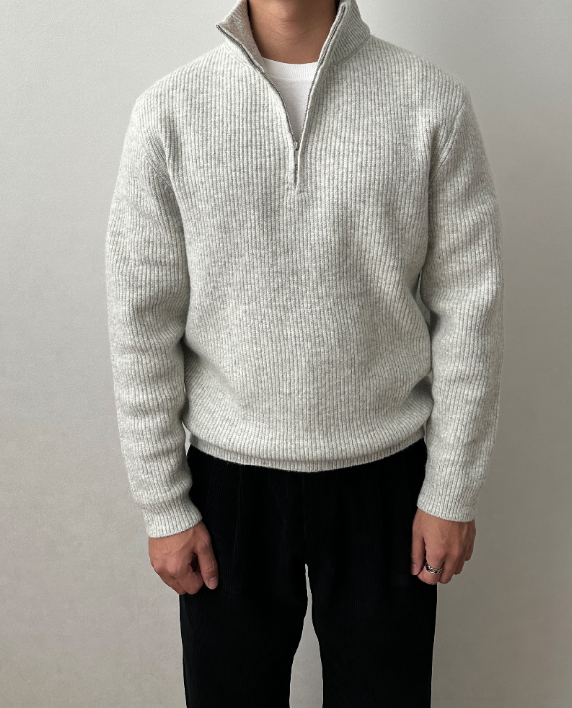 Light gray quarter-zip knit sweater with a stand collar, ribbed cuffs, and a relaxed fit, paired with black trousers.