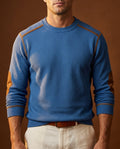 Blue textured crew neck knit sweater with contrast shoulder trim, long sleeves, and ribbed cuffs, paired with light-colored trousers.