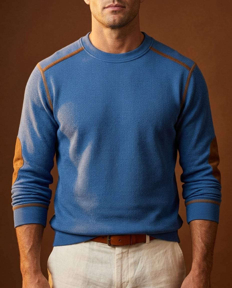 Blue textured crew neck knit sweater with contrast shoulder trim, long sleeves, and ribbed cuffs, paired with light-colored trousers.