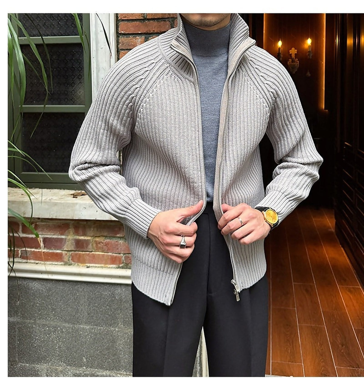 Light gray ribbed knit zip-up cardigan in a relaxed fit, layered over a grey turtleneck and black trousers.