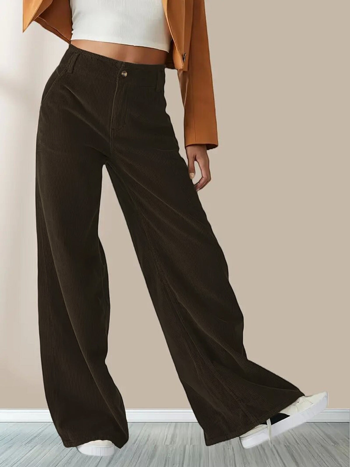 Dark brown wide-leg corduroy pants with a button-zip fly, slant pockets, and a relaxed, flowing fit worn with sneakers.