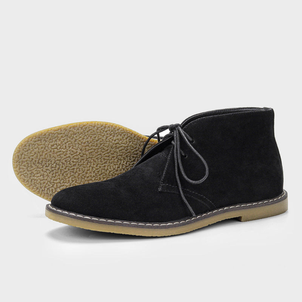 Black suede chukka boots featuring a rounded toe, short lace-up front, contrast panel stitching, and a textured gum sole.