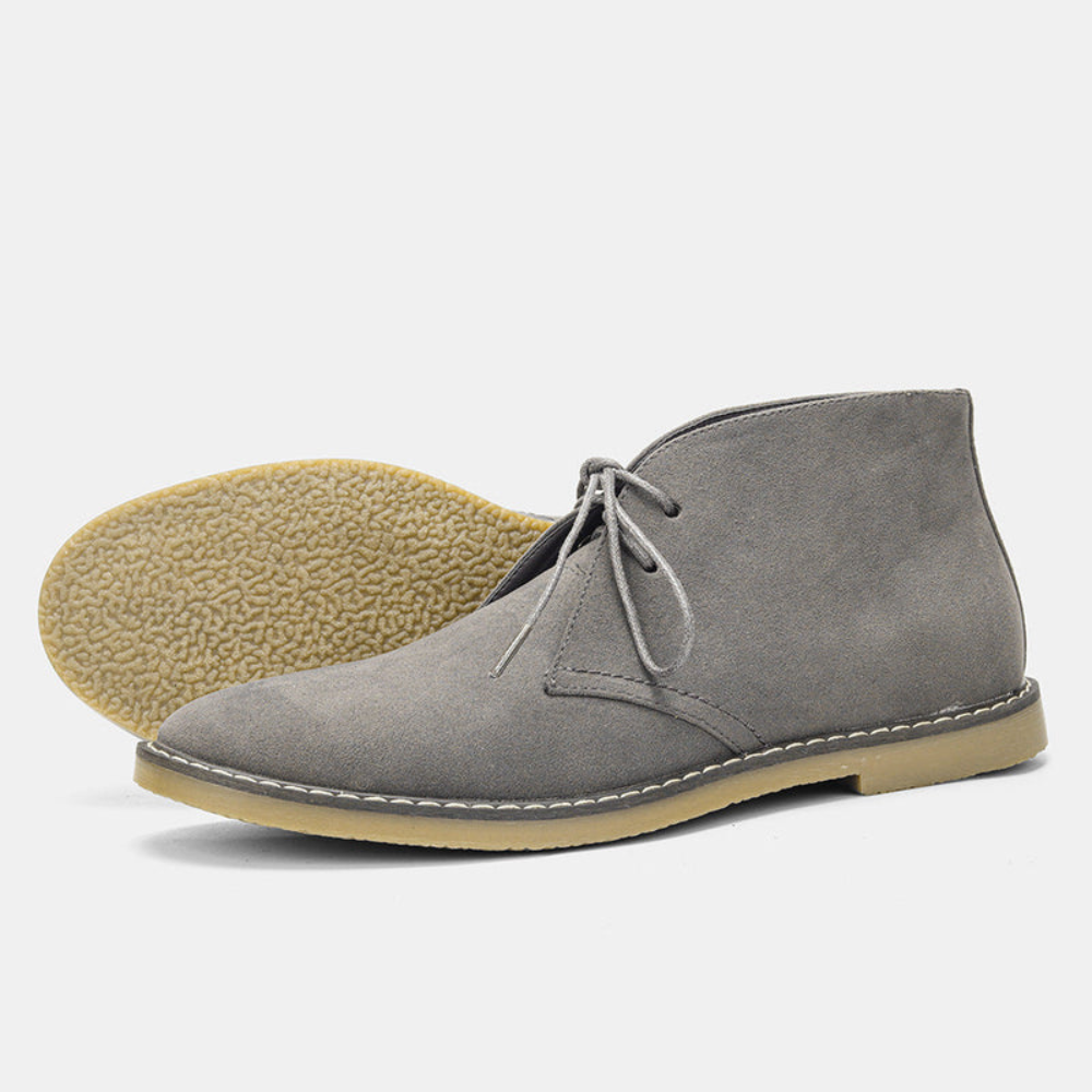 Grey suede chukka boots with a rounded toe, short lace run, contrast panel stitching, and a textured gum sole.