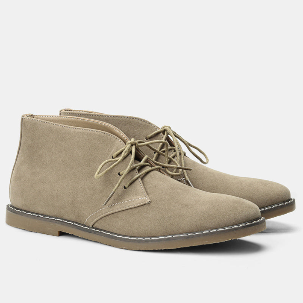 Taupe suede chukka boots featuring a rounded toe, short lace-up front, and contrast panel stitching on a low stacked heel.