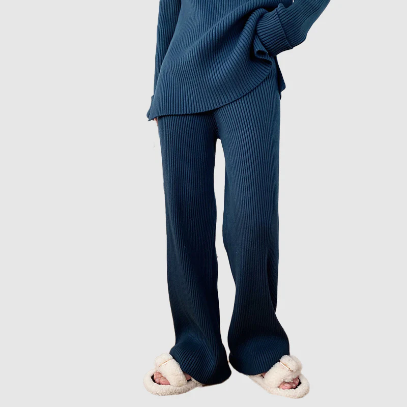 Lower-body view of a model standing in a blue ribbed knit lounge set featuring wide-leg pants and cozy slippers.