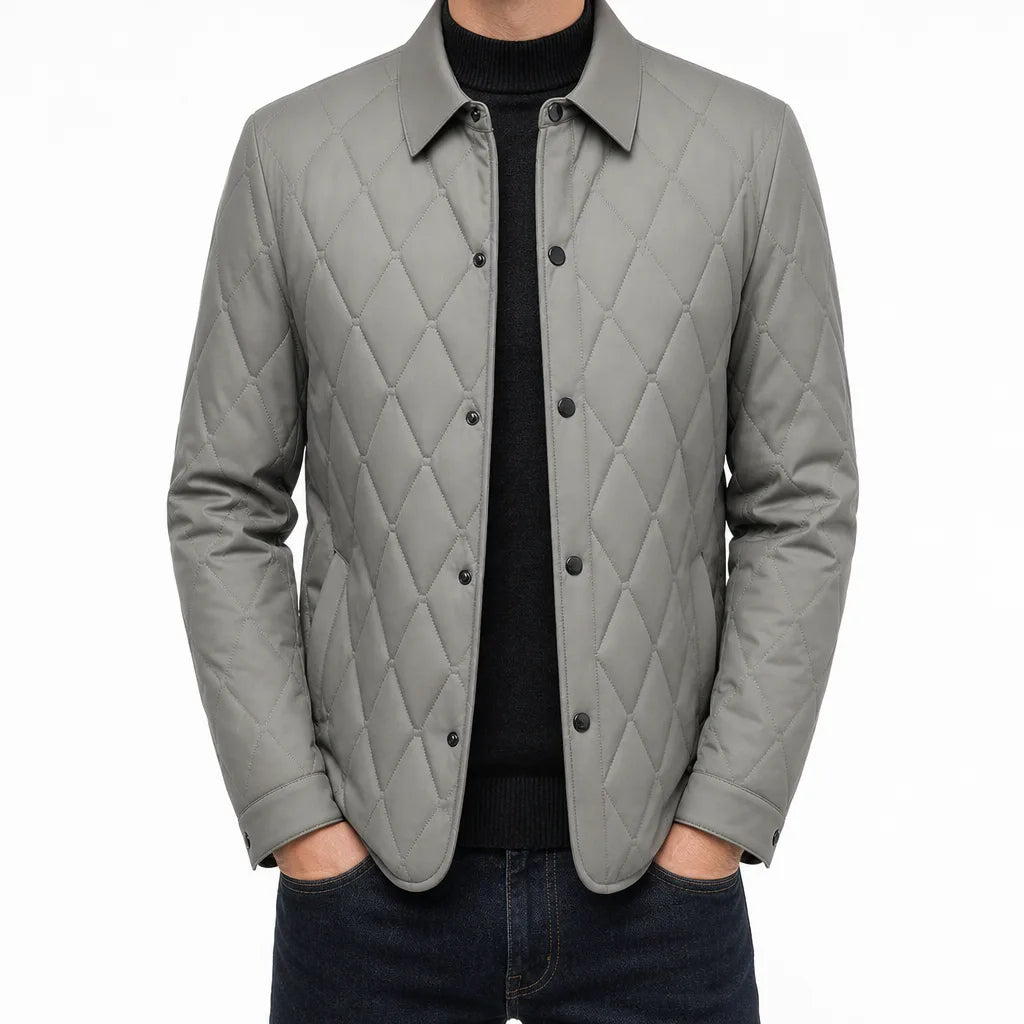 Man wearing a light gray quilted button-front jacket with a classic collar, diamond quilted front, and long sleeves layered over a black shirt.