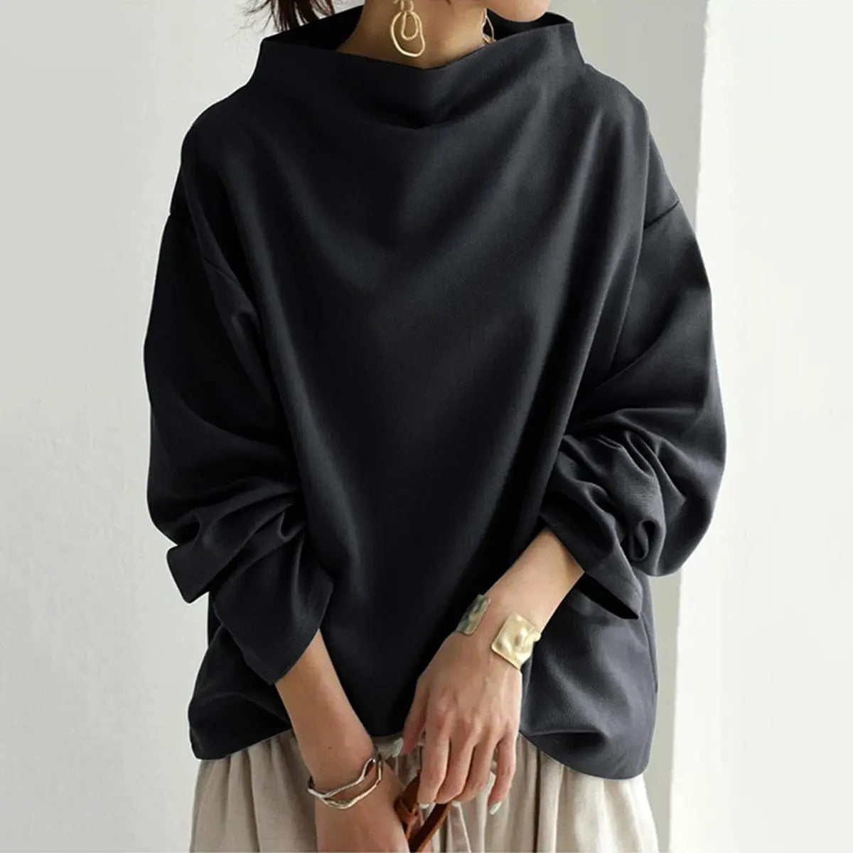 Black oversized mock neck sweatshirt with dropped shoulders and ribbed cuffs, worn with neutral-toned trousers.