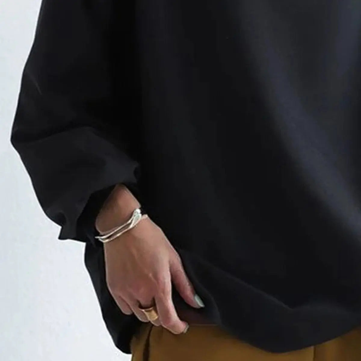 Close-up of the black oversized sweatshirt showing the relaxed hem, sleeve cuff, and soft fabric drape.