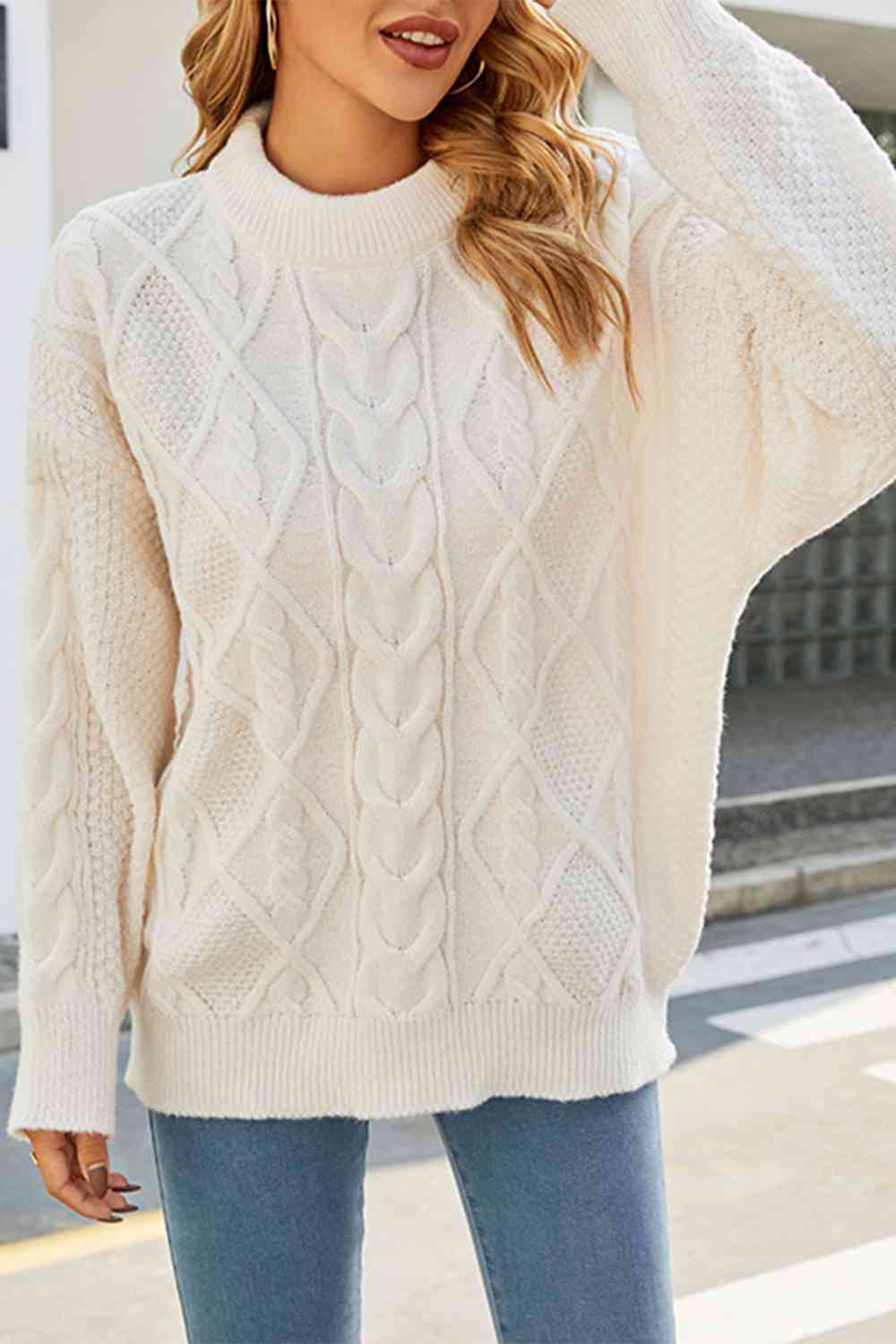 Off-white cable-knit crewneck sweater with a relaxed, drop-shoulder fit and intricate braided texture.