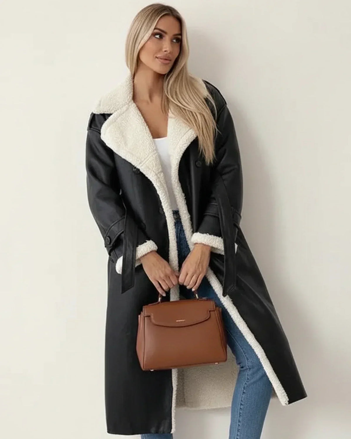 Black longline coat with white shearling trim, wide collar, and double-breasted fit worn over jeans and a white top.
