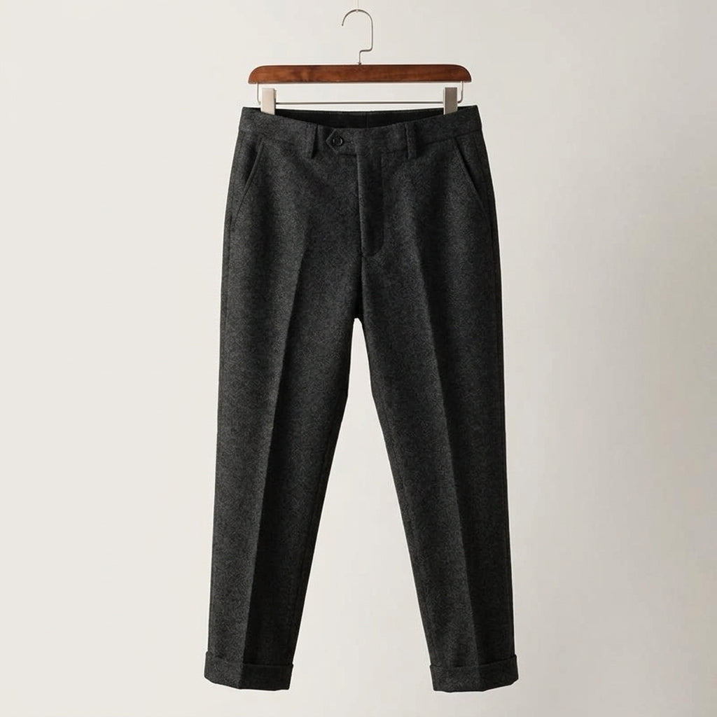 Black slim-fit wool-blend trousers featuring subtle pleats and a tailored, cuffed hem on a wooden hanger.