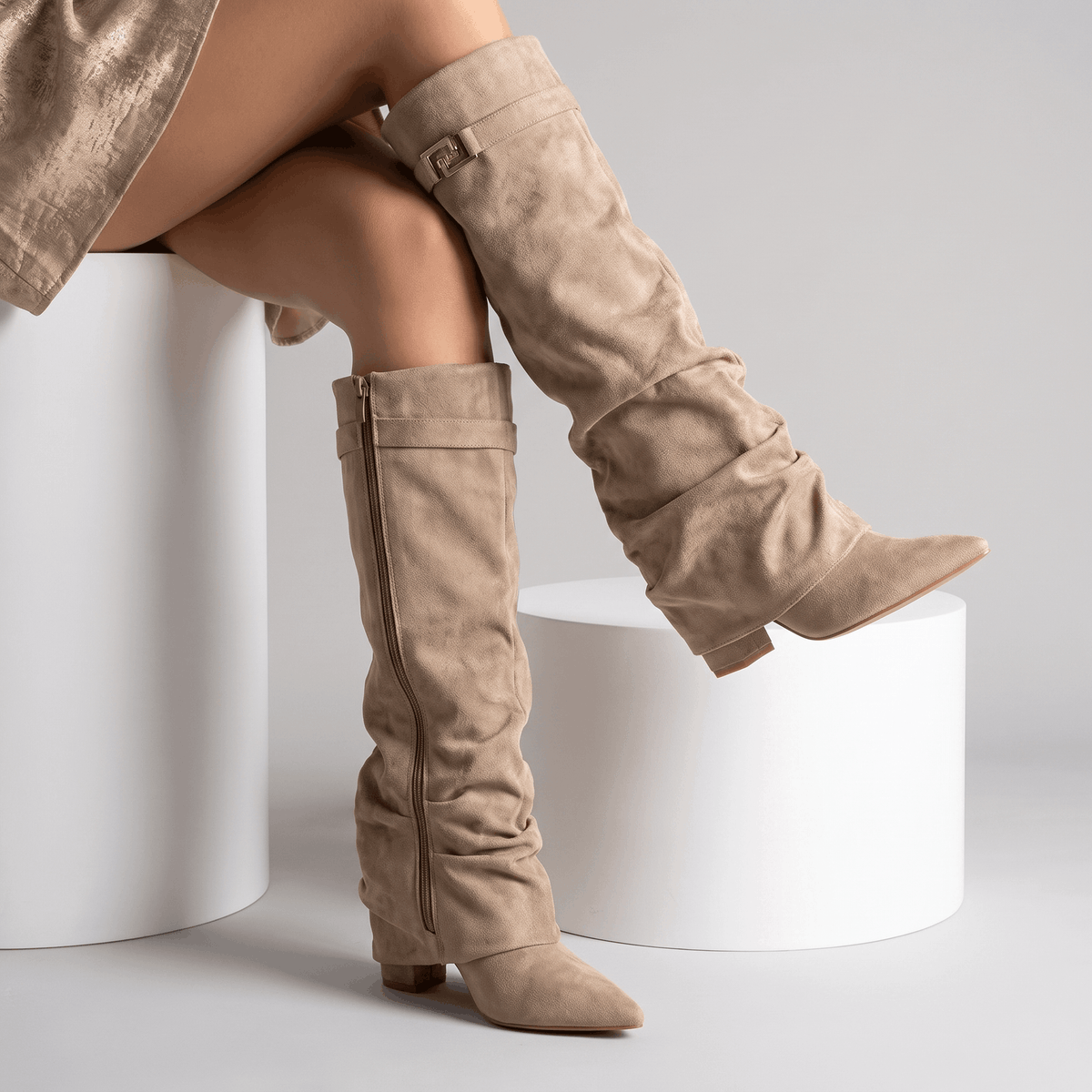 Beige slouchy fold-over boots worn by a female model in a seated pose