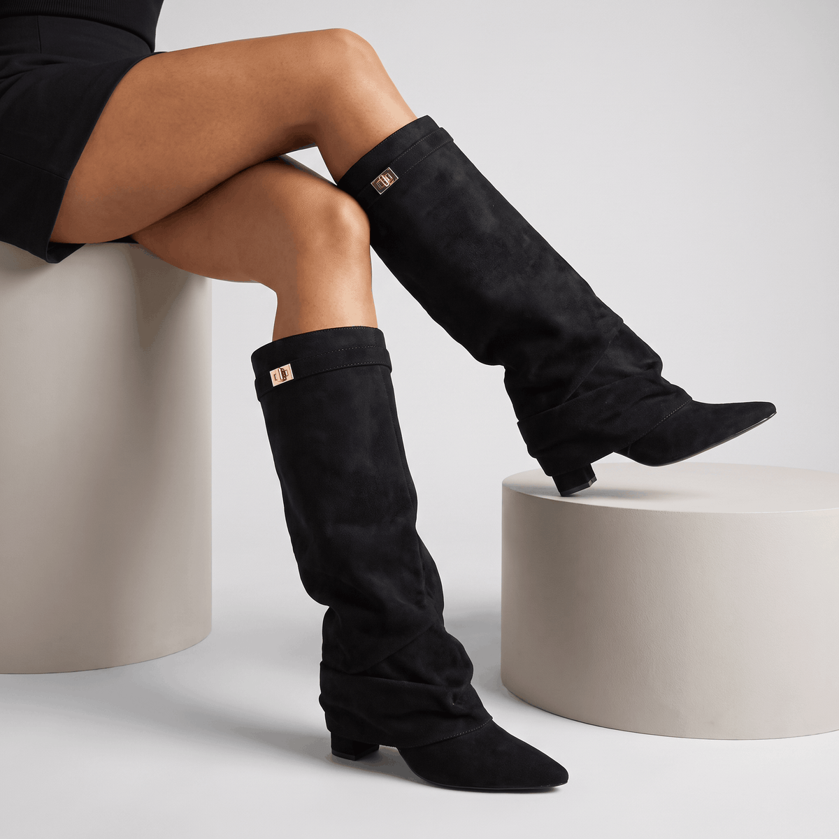 Black slouchy fold-over boots worn by a female model in a seated pose