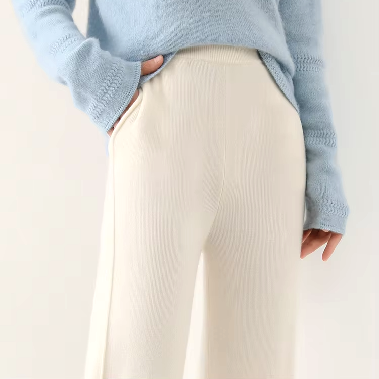 Close-up view of the elastic waistband and upper fit of off-white straight-leg wool knit pants, paired with a light blue top.