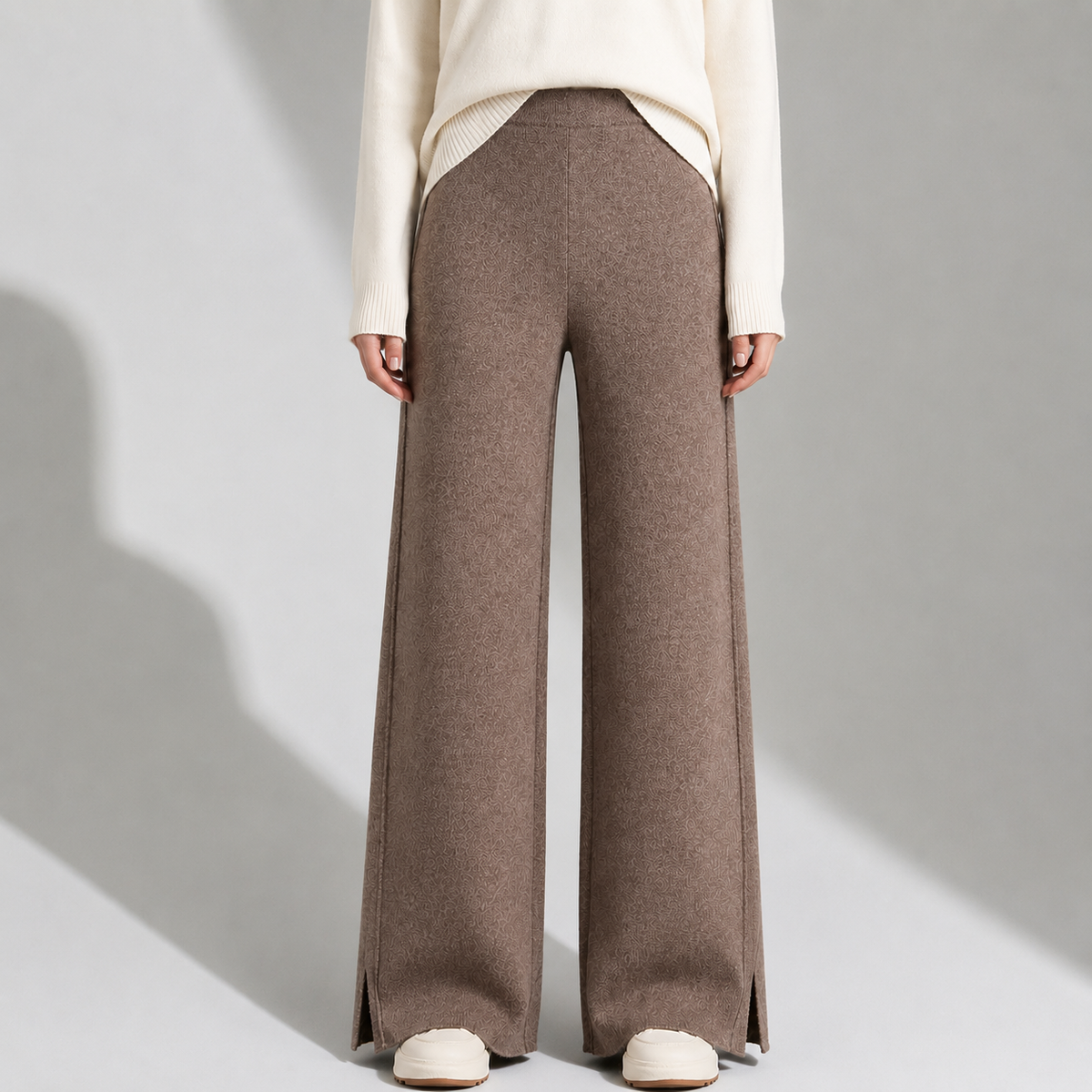Front view of a model wearing straight-leg brown wool knit pants featuring an elastic waistband and side slit hems, paired with a white sweater.