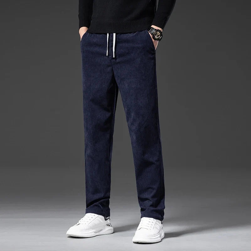 Navy blue stretch corduroy pants with a straight-leg fit, elastic drawstring waist, and ribbed texture worn with white sneakers.