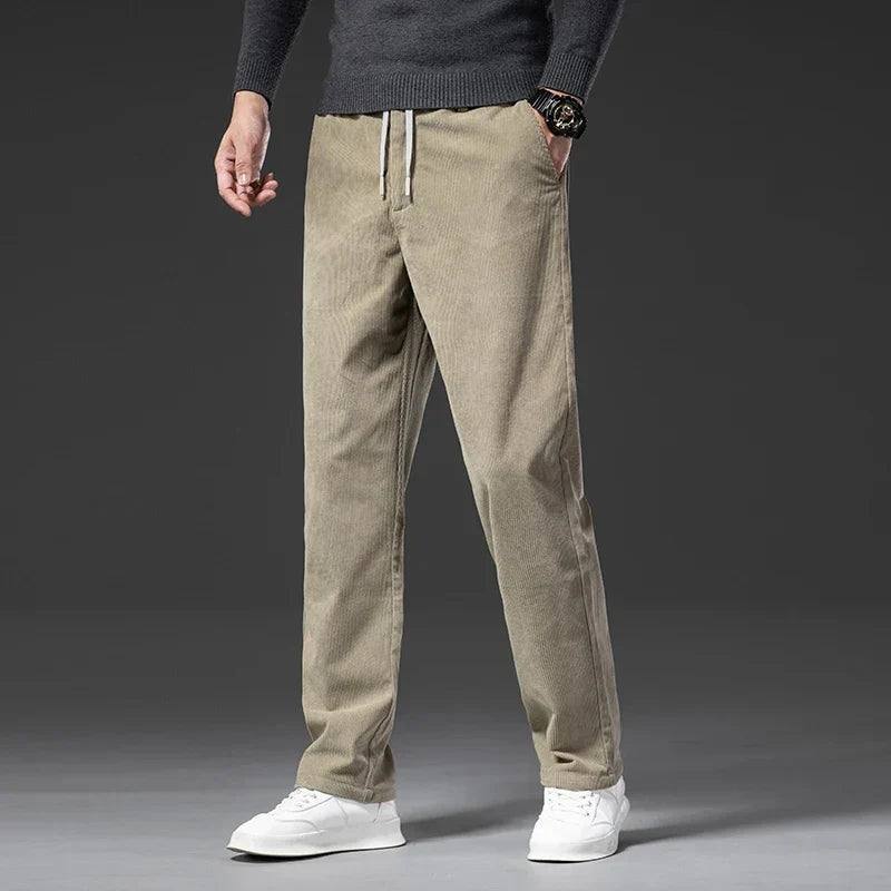 Tan stretch corduroy pants with an elastic drawstring waist and straight-leg fit, paired with a grey sweater and white sneakers.
