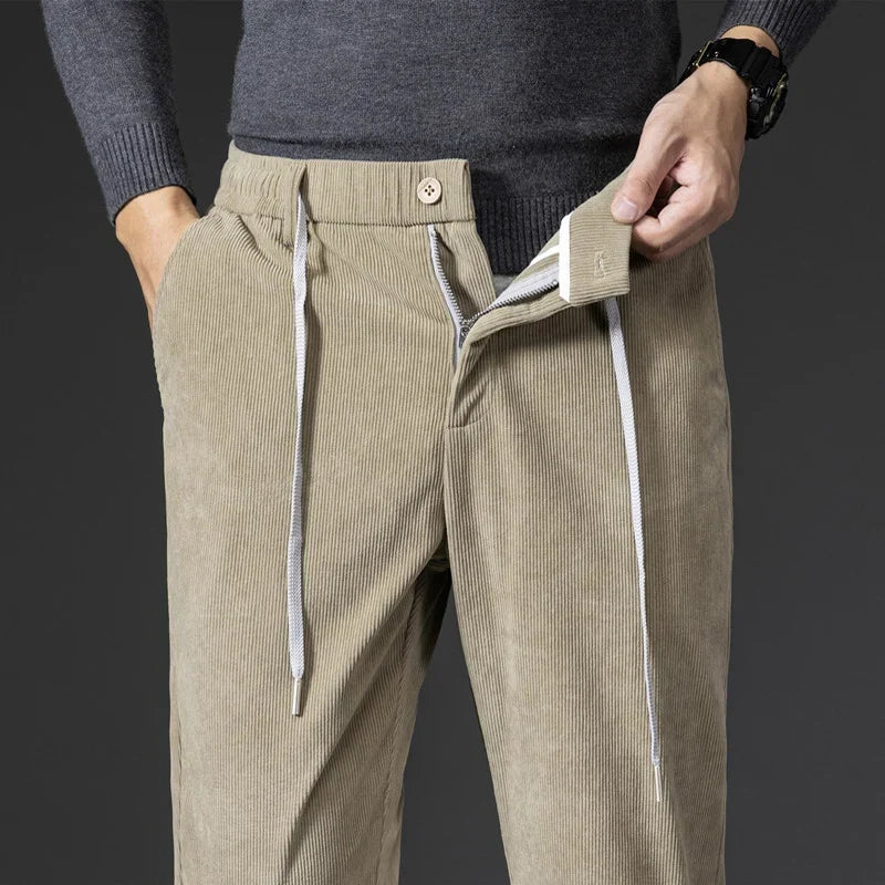 Beige stretch corduroy pants featuring an elastic drawstring waist, straight-leg fit, and a zippered fly closure.