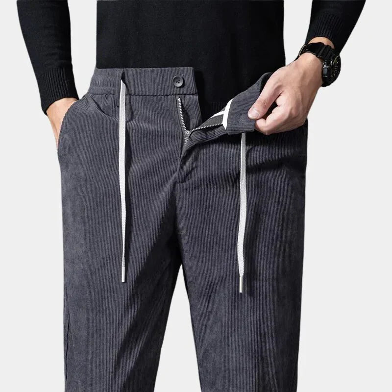 Charcoal gray stretch corduroy pants featuring a straight-leg cut, elastic drawstring waist, and a secure button-zip fly.